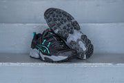 black asics with teal and grey accents on a set of stairs with one shoe showing the sole of the shoe